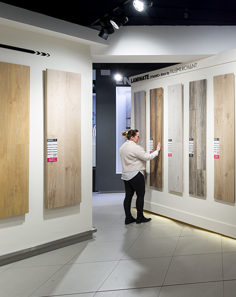 Person examining laminate flooring samples displayed on a showroom wall.