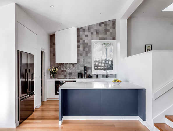 Modern kitchen with a blue island, white countertops, stainless steel appliances, and wood flooring.