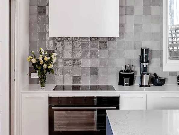 Modern kitchen with glossy tiled backsplash, white cabinets, black stove, and a vase of flowers on the counter.