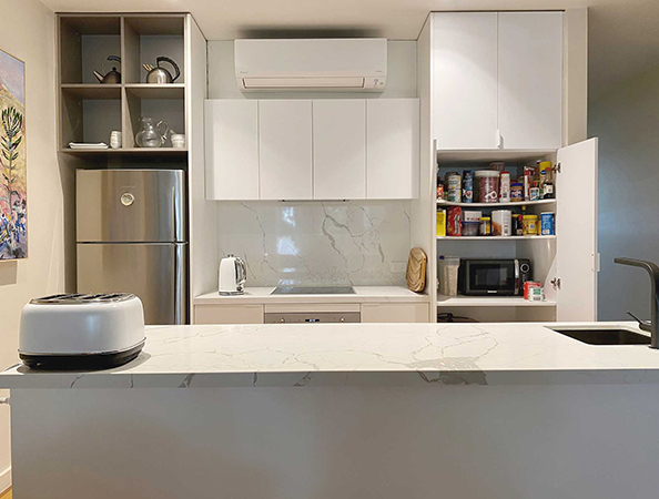 Modern kitchen with white cabinets, open pantry, fridge, toaster, and marble countertop.