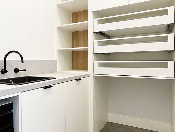Modern white kitchen with black faucet, open drawers, and wood shelving. Minimalist design.