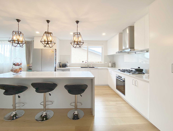 Modern kitchen with white cabinets, island with stools, pendant lights, and stainless steel appliances.