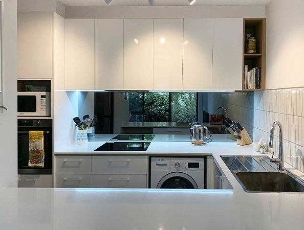 Modern kitchen with white cabinets, built-in oven, induction cooktop, washing machine, and stainless steel sink. Modern kitchen with white cabinets, built-in oven, induction cooktop, washing machine, and stainless steel sink.