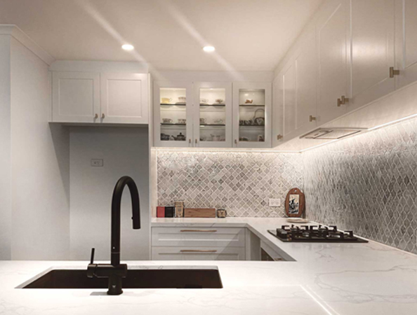 Modern kitchen with white cabinets, black faucet, marble countertops, and a tiled backsplash under warm lighting.