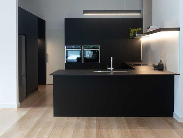 Modern kitchen with black cabinetry, island counter, built-in appliances, and wooden flooring.