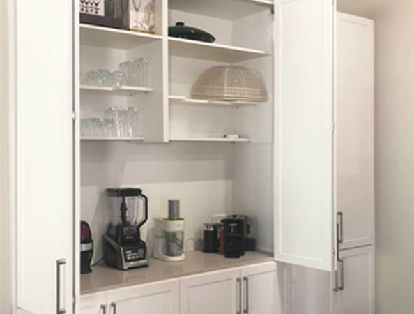 Open white kitchen cabinet with glassware, a blender, coffee maker, and closed cabinet doors.