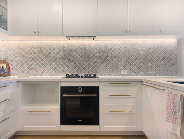 Modern kitchen with white cabinets, patterned backsplash, and a black oven with a gas cooktop.
