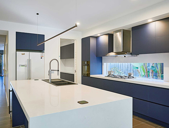 Modern kitchen with white island, built-in sink, dark blue cabinets, stainless steel appliances, and large window.
