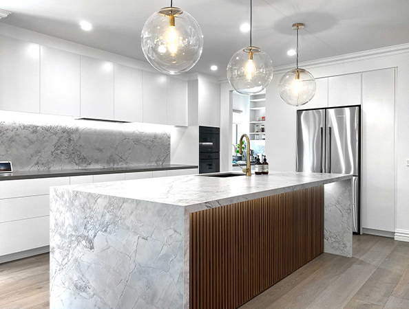 Modern kitchen with marble island, globe pendant lights, white cabinets, and stainless steel appliances.