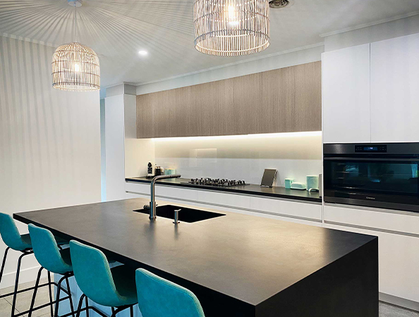 Modern kitchen with island, sleek black countertop, teal barstools, pendant lights, and built-in oven.