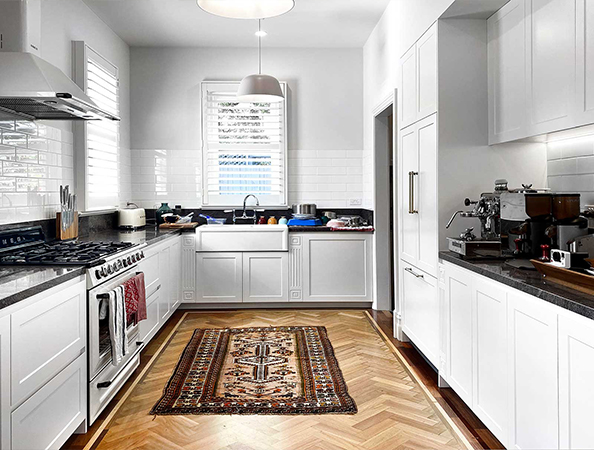 A bright kitchen with white cabinets, a farmhouse sink, and a patterned rug on wooden flooring.