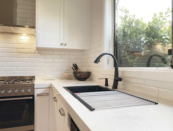 Modern kitchen with white cabinets, black faucet, and large window overlooking greenery.