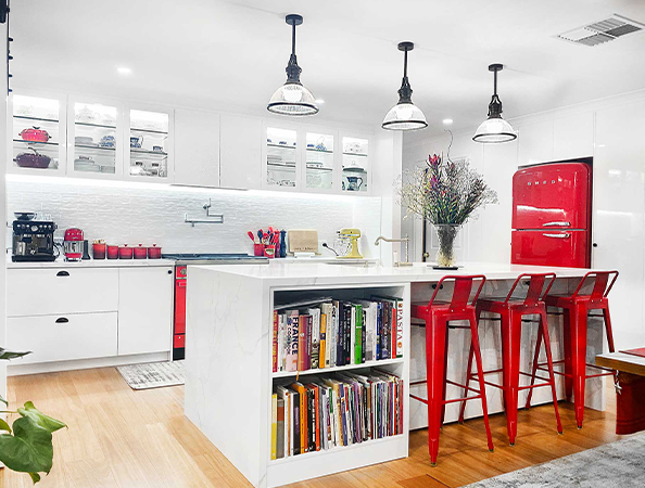 Modern kitchen with a red refrigerator, white cabinets, an island with bookshelves, and red bar stools.