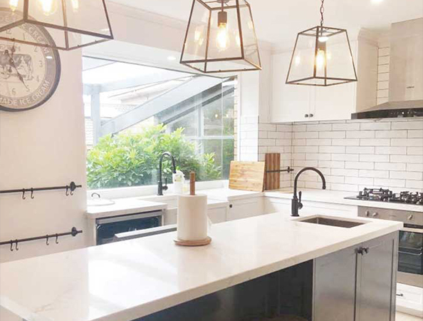Bright kitchen with white countertops, black fixtures, hanging lantern lights, and a window overlooking greenery.