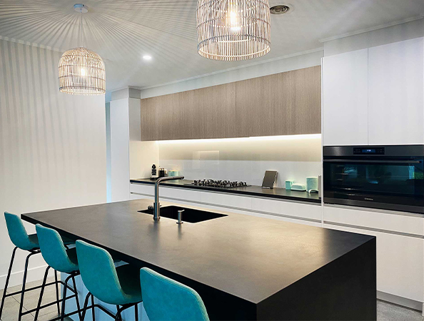 Modern kitchen with a black island, teal high chairs, pendant lights, and sleek white and wooden cabinets.