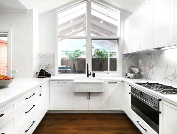 Bright kitchen with white cabinets, marble backsplash, farmhouse sink, and large window. Wood floor and skylight roof. Bright kitchen with white cabinets, marble backsplash, farmhouse sink, and large window. Wood floor and skylight roof.
