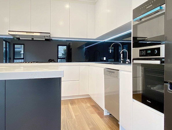 Modern kitchen with white cabinets, stainless steel appliances, and wood flooring. Black backsplash adds contrast. Modern kitchen with white cabinets, stainless steel appliances, and wood flooring. Black backsplash adds contrast.