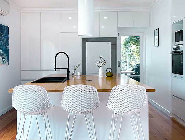 Modern kitchen with white cabinetry, wood countertop island, black faucet, and white bar stools. Bright and minimalistic.