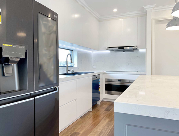 Modern kitchen with white cabinets, black fridge, marble countertops, and wood flooring. Modern kitchen with white cabinets, black fridge, marble countertops, and wood flooring.