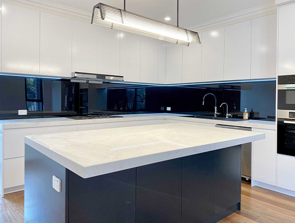 Modern kitchen with white cabinets, black backsplash, and a large island with white countertop under a sleek light fixture. Modern kitchen with white cabinets, black backsplash, and a large island with white countertop under a sleek light fixture.