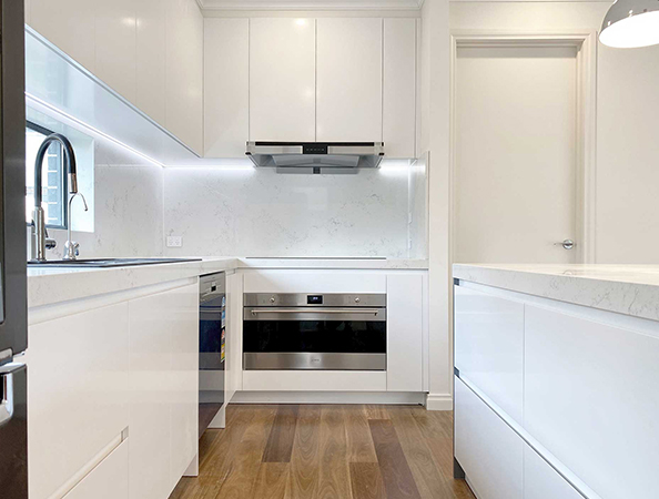 Modern white kitchen with wooden floor, built-in oven, stovetop, and overhead cabinets, featuring bright lighting. Modern white kitchen with wooden floor, built-in oven, stovetop, and overhead cabinets, featuring bright lighting.