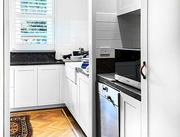 Compact kitchen with white cabinets, black countertops, a microwave, dishwasher, and window with blinds. Compact kitchen with white cabinets, black countertops, a microwave, dishwasher, and window with blinds.
