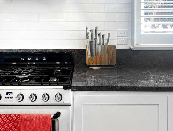 Kitchen with a black SMEG gas stove, red towel, knife set on counter, and white subway tile backsplash. Kitchen with a black SMEG gas stove, red towel, knife set on counter, and white subway tile backsplash.