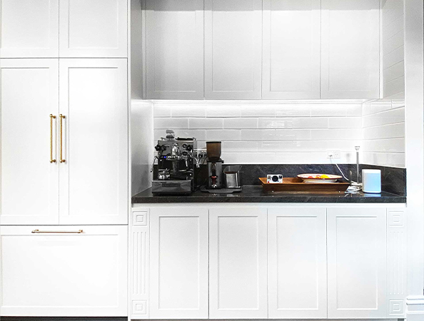 Modern white kitchen with a coffee maker and tray on a black countertop, beneath a tiled backsplash.