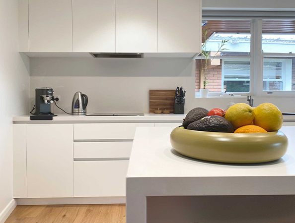 Modern kitchen with white cabinets, a countertop appliance, and a bowl of fruits on the island. Natural light from window. Modern kitchen with white cabinets, a countertop appliance, and a bowl of fruits on the island. Natural light from window.