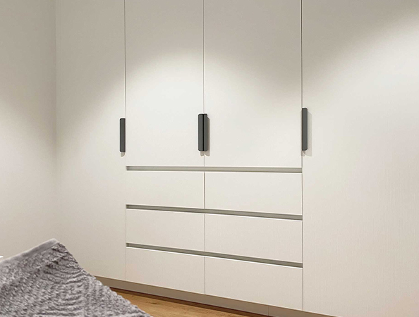 White built-in wardrobe with black handles, featuring three tall doors and four horizontal drawers. White built-in wardrobe with black handles, featuring three tall doors and four horizontal drawers.