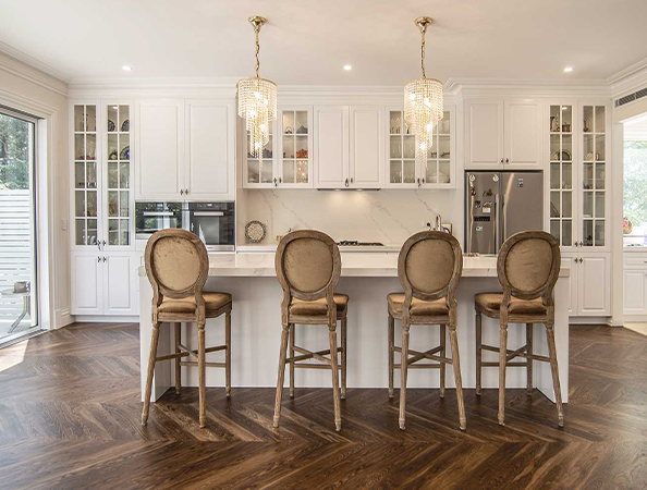 Elegant kitchen with a marble island, four upholstered chairs, pendant lights, wood flooring, and glass cabinet doors. Elegant kitchen with a marble island, four upholstered chairs, pendant lights, wood flooring, and glass cabinet doors.