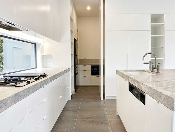 Modern kitchen with white cabinets, gray countertops, gas stove, and a large island with a sink. Natural light in room.