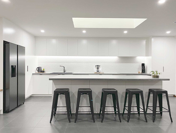 Modern kitchen with white cabinets, a long island with five black stools, and a skylight above.