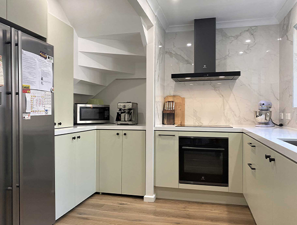 Modern kitchen with a fridge, microwave, coffee maker, oven, and sleek countertops, featuring light green cabinets.