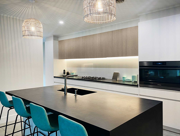 Modern kitchen with a black island, teal bar stools, two pendant lights, and built-in oven.