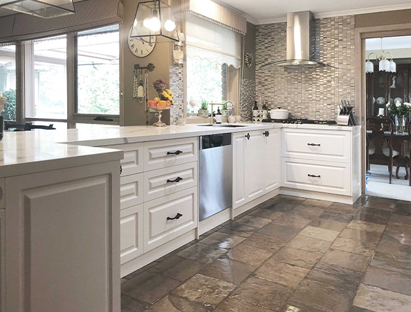 Bright kitchen with white cabinets, stainless steel appliances, and a stone tile floor. Large windows in the background. Bright kitchen with white cabinets, stainless steel appliances, and a stone tile floor. Large windows in the background.