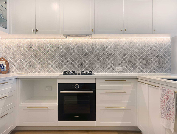 Modern kitchen with white cabinets, patterned backsplash, black oven, and gas stove. Tea towel on dishwasher handle. Modern kitchen with white cabinets, patterned backsplash, black oven, and gas stove. Tea towel on dishwasher handle.