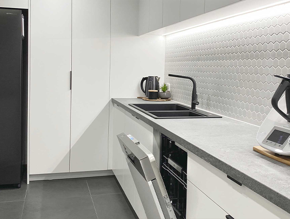 Modern kitchen with a grey countertop, open dishwasher, black sink, and geometric backsplash tiles. Modern kitchen with a grey countertop, open dishwasher, black sink, and geometric backsplash tiles.
