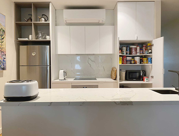 Modern kitchen with a marble island, open pantry, white cabinets, fridge, and a toaster on the counter.