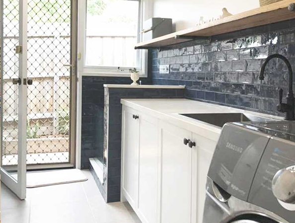 Laundry room with a washing machine, white cabinetry, dark blue brick backsplash, and a screen door.