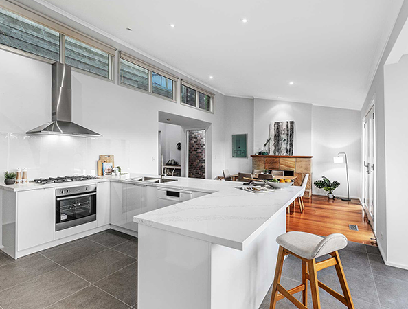 Modern kitchen with white cabinets, marble countertops, bar stool, and dining area in a bright open-concept space.