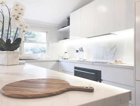 Modern kitchen with white cabinets, marble countertops, a wooden cutting board, and a vase of white orchids. Modern kitchen with white cabinets, marble countertops, a wooden cutting board, and a vase of white orchids.