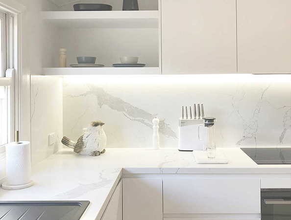 Modern kitchen with white countertops and cabinets, a bird sculpture, knife set, and coffee maker. Natural light streams in. Modern kitchen with white countertops and cabinets, a bird sculpture, knife set, and coffee maker. Natural light streams in.
