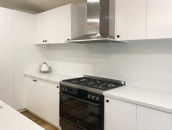 Modern kitchen with white cabinets, a stainless steel range hood, black oven, and a white electric kettle on the counter. Modern kitchen with white cabinets, a stainless steel range hood, black oven, and a white electric kettle on the counter.