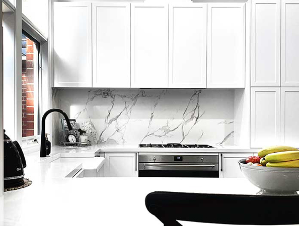 A modern white kitchen with marble backsplash, black faucet, and a bowl of fruit on the counter. A modern white kitchen with marble backsplash, black faucet, and a bowl of fruit on the counter.