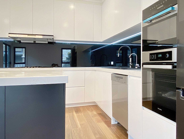 Modern kitchen with white cabinets, black backsplash, built-in appliances, and wood flooring.
