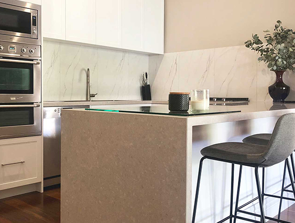 Modern kitchen with marble backsplash, sleek oven, and island with bar stools and decorative vase.