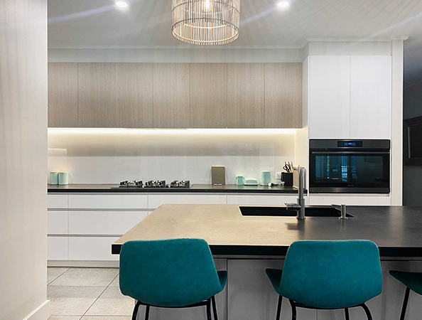 Modern kitchen with teal chairs, black countertop, built-in oven, and overhead lighting.