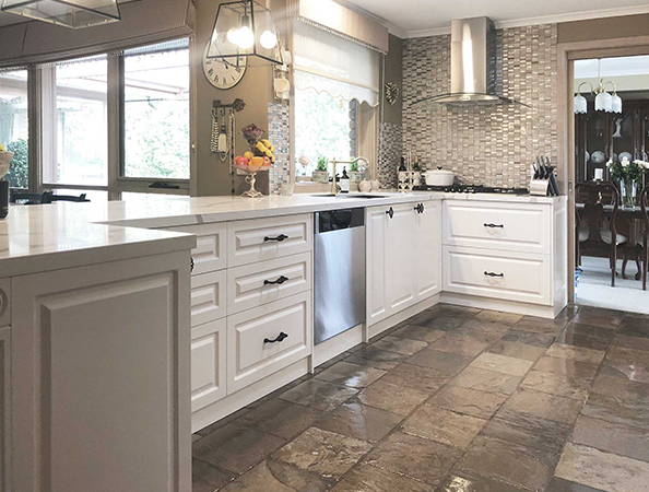 Modern kitchen with white cabinets, stainless steel appliances, and a tile floor. Bright light from large windows.
