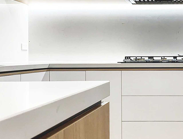 Modern kitchen with white countertops, wooden cabinets, and a gas stove on the right.